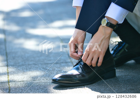 ビジネスシューズの靴紐を結ぶスーツの若い男性の足元 128432686