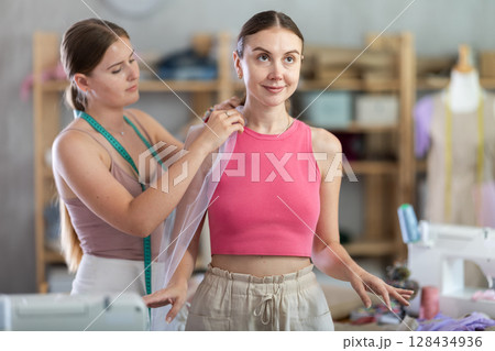 Young female seamstress adjusting clothes on adult woman 128434936
