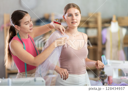 dressmaker is trying on a sample of clothes with a client 128434937