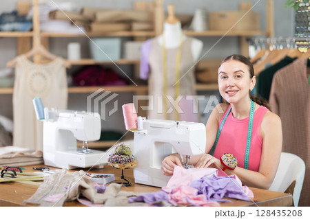 Woman seamstress sews on sewing machine in workshop 128435208