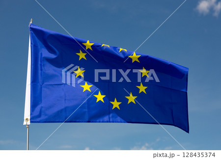 Flag of European Union flies on flagpole against blue sky 128435374