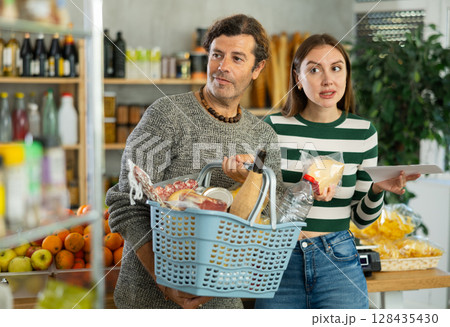 Couple following shopping list while choosing foods in grocery store 128435430