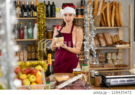 Half-naked girl in apron and Santa hat stands in store near counter Half-naked girl in apron and Santa hat stands in store near counter 128435472