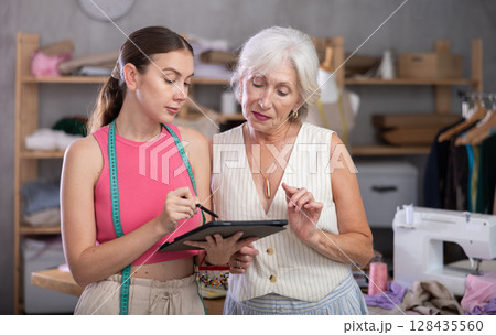 Elderly and adult seamstresses drawing pattern on tablet 128435560