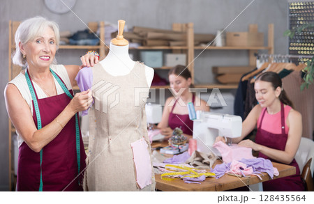 Woman and girl tailors sewing, senior female designer work with mannequin. Woman and girl tailors sewing, senior female designer work with mannequin. 128435564