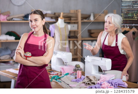 Senior woman head of sewing workshop yells at her subordinate female seamstress, 128435579