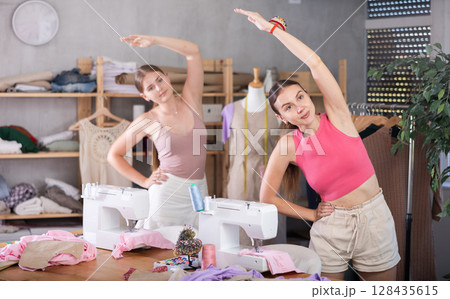 Young and adult women doing warm-up exercises in sewing workshop 128435615