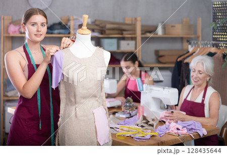 Mature head of manufacturing and female assistant sewing, young designer work with mannequin. Mature head of manufacturing and female assistant sewing, young designer work with mannequin. 128435644