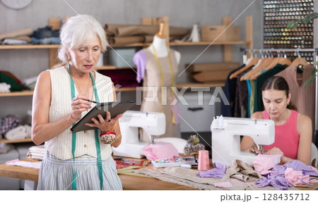 Adult seamstress sewing woman assistant drawing pattern on tablet 128435712