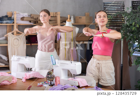 Young and adult women doing warm-up exercises in sewing workshop Young and adult women doing warm-up exercises in sewing workshop 128435729
