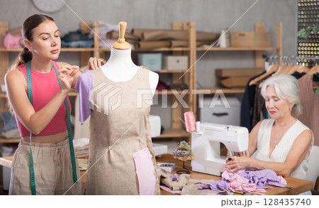 Senior woman tailor busy with sewing machine, female employee work with mannequin Senior woman tailor busy with sewing machine, female employee work with mannequin 128435740