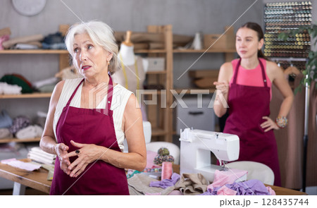 Adult woman scolding elderly woman in sewing workshop 128435744