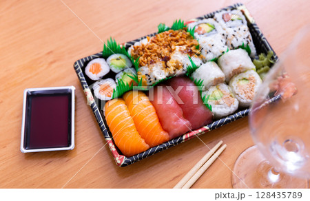 Sushi set roll of uramaki and nigiri is decorated with imitation grass, served on rectangular plate Sushi set roll of uramaki and nigiri is decorated with imitation grass, served on rectangular plate 128435789