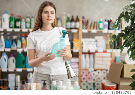 Young woman chooses cleaning spray in store Young woman chooses cleaning spray in store 128435793