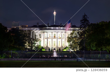 Illuminated night view of the White House in Washington, D.C., with the American flag flying beside the iconic neoclassical structure, symbolizing national leadership and heritage 128436059