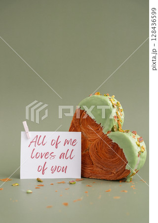 ALL OF ME LOVES ALL OF YOU greeting card note Valentines day celebration idea Heart shaped pistachio croissant on green background with copy space. Puff pastry trendy sweet dessert bakery. Creamy 128436599