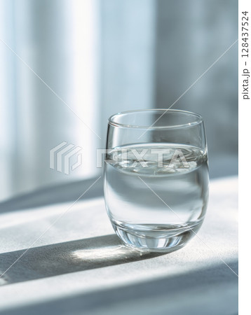 A glass filled with warm salt water sits on a clean surface beside an instruction card for gargling, illuminated by soft, natural light. 128437524