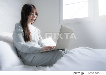 ベッドの上でパソコンをする俯く女性　ライフスタイルやフリーランス、働き方や忙しい仕事のイメージ	 128438538