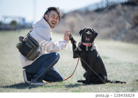 青空の河川敷で散歩を楽しむ男性と犬 見つめ合うハイタッチやお手 信頼、親友やバディのイメージ 青空の河川敷で散歩を楽しむ男性と犬 見つめ合うハイタッチやお手 信頼、親友やバディのイメージ 128438829