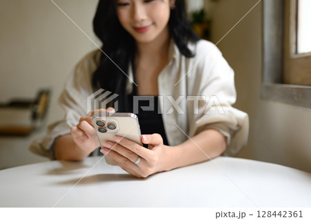 Close up of a woman hands holding and using a smartphone while seated at a cafe table Close up of a woman hands holding and using a smartphone while seated at a cafe table 128442361