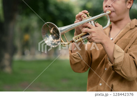 Young man playing trumpet in a park, enjoying music in a peaceful outdoor 128442376