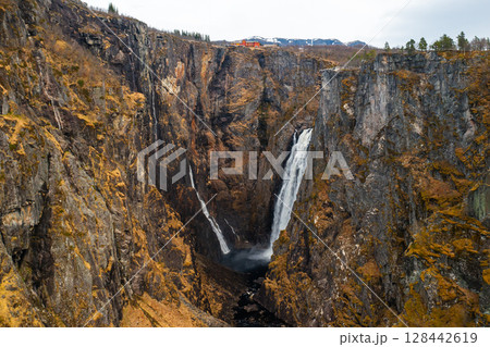 Voringsfossen waterfall with powerful stream cascading down deep gorge framed by imposing barren cliffs. Distant mountain under sky in Norway Voringsfossen waterfall with powerful stream cascading down deep gorge framed by imposing barren cliffs. Distant mountain under sky in Norway 128442619