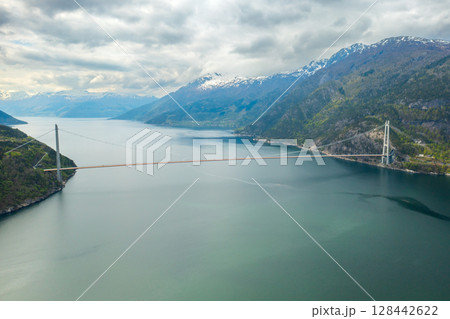 Hardanger Bridge gracefully arches over fjord calm waters with sailing sizable cruise liner. Majestic mountains encapsulates serene beauty of Norway 128442622