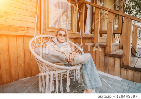 Woman Relaxing in a Hanging Chair on a Wooden Porch 128445397