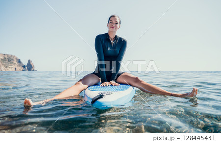 Woman Paddleboard Ocean Smiling woman in wetsuit sits on paddleboard in ocean. 128445431
