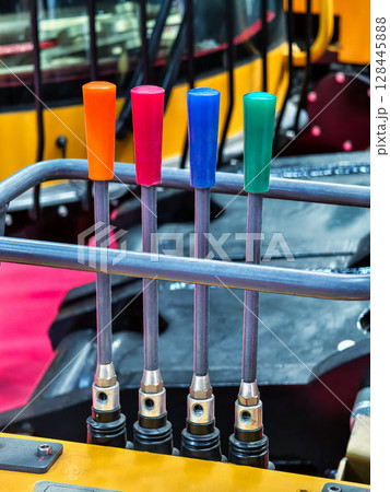 Colorful hydraulic levers arranged in a construction vehicle at a worksite in daylight 128445888