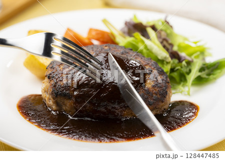 デミグラスソースのハンバーグをフォークとナイフで切る瞬間 デミグラスソースのハンバーグをフォークとナイフで切る瞬間 128447485