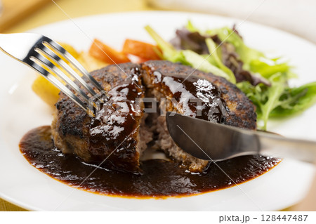 デミグラスソースのハンバーグをフォークとナイフで切る瞬間 128447487