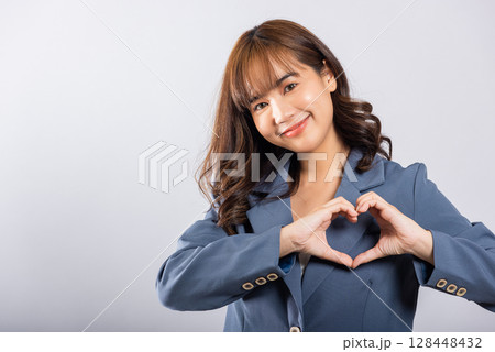 A confident business woman wear suit smiles and creates a heart symbol with two hands on white background. Asian portrait of a beautiful young female expressing love and happiness for Valentine's Day A confident business woman wear suit smiles and creates a heart symbol with two hands on white background. Asian portrait of a beautiful young female expressing love and happiness for Valentine's Day 128448432