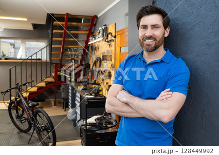 Man bike mechanic standing workshop entrance wearing blue t-shirt Man bike mechanic standing workshop entrance wearing blue t-shirt 128449992