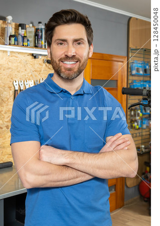 Bearded man mechanic standing with arms crossed in workshop Bearded man mechanic standing with arms crossed in workshop 128450048