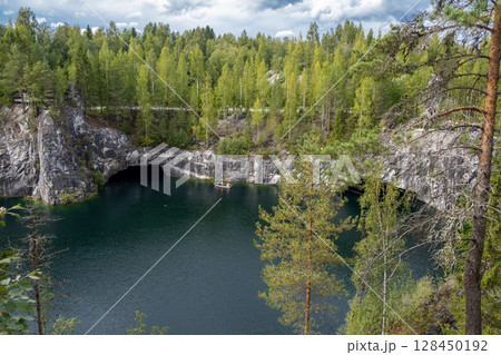 Visitors admire the stunning Marble Canyon in Ruskeala Mountain Park, where lush trees frame the serene blue waters below. Visitors admire the stunning Marble Canyon in Ruskeala Mountain Park, where lush trees frame the serene blue waters below. 128450192