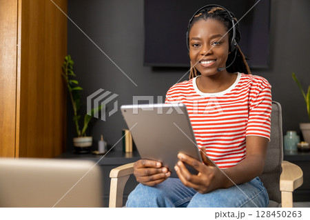 Cute african american young woman in headphones with a tablet in hands 128450263