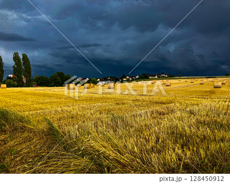 Gewitterwolken, starker Sturm und Winde über dem ländlichen Landschaft mit Heuballen in der hessischen Engelhelms bei Fulda. Gewitterwolken und stürmischer Himmel über einem Feld mit goldenem Hafer 128450912