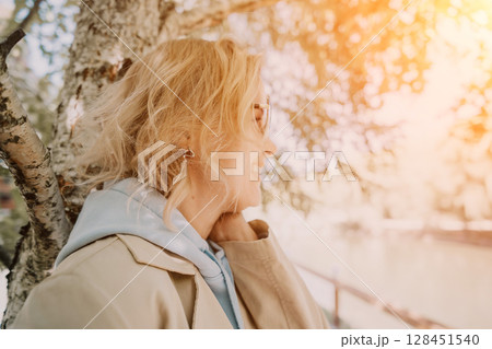 Woman, Tree, Sunset - A woman in a tan coat stands by a tree, looking out at a sunset. 128451540