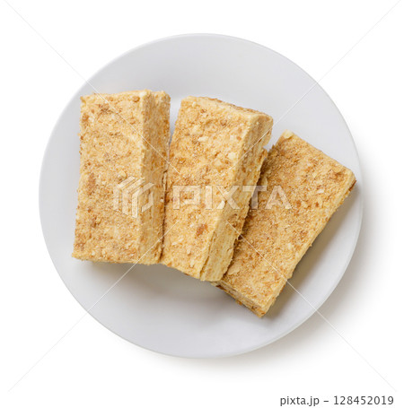 Pieces of napoleon cake on a plate on a white background. Top view 128452019