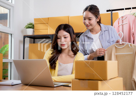 Two young asian businesswoman checking order clothes of customer for laptop computer. Two young asian businesswoman checking order clothes of customer for laptop computer. 128452177