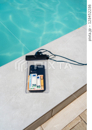 Waterproof case with money and a smartphone on the background of the pool on a sunny summer day 128452286