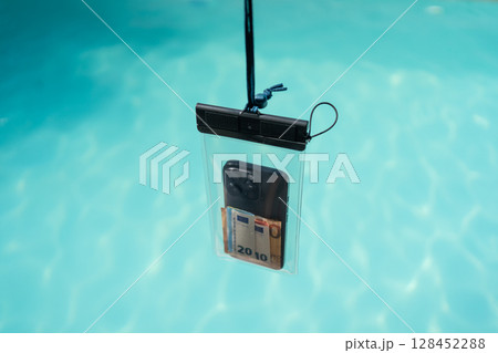 Waterproof case with money and a smartphone on the background of the pool on a sunny summer day Waterproof case with money and a smartphone on the background of the pool on a sunny summer day 128452288