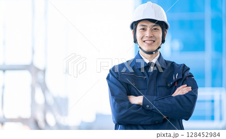 腕組みをしながら作業着とヘルメットを被った笑顔の男性 128452984