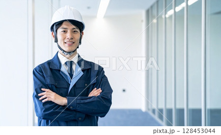 腕組みをしてヘルメットを被った作業服の男性 128453044