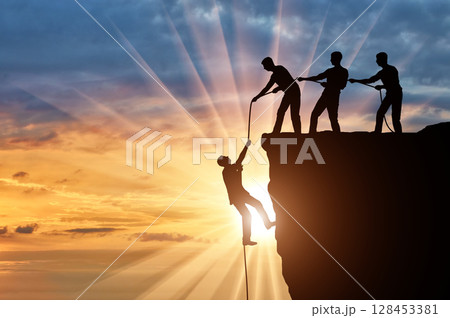 Silhouette of three climbers pulling out of the cliff of a man. Silhouette of three climbers pulling out of the cliff of a man. 128453381