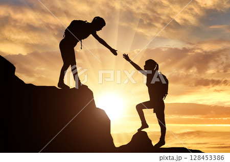 Silhouettes of two women climber climb the mountain helping each other 128453386