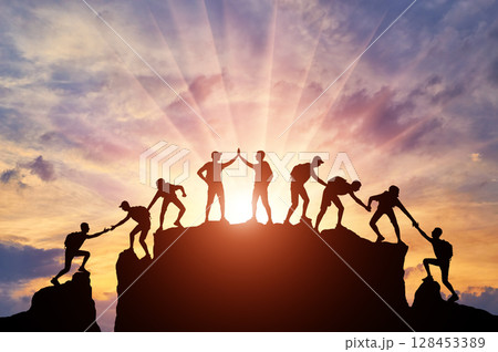 Silhouette of climbers who climbed to the top of the mountain thanks to mutual assistance and teamwork Silhouette of climbers who climbed to the top of the mountain thanks to mutual assistance and teamwork 128453389