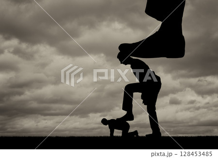 Silhouette of a large leg presses on a man who also presses his foot on another man lying on the ground 128453485