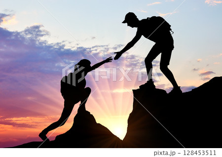 Silhouette of a male climber giving a helping hand to a woman 128453511